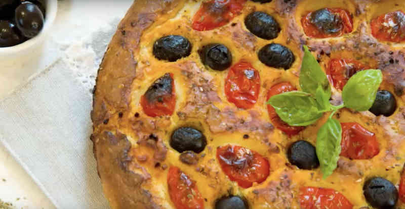 Focaccia pugliese dorata condita con pomodorini, olive nere e origano