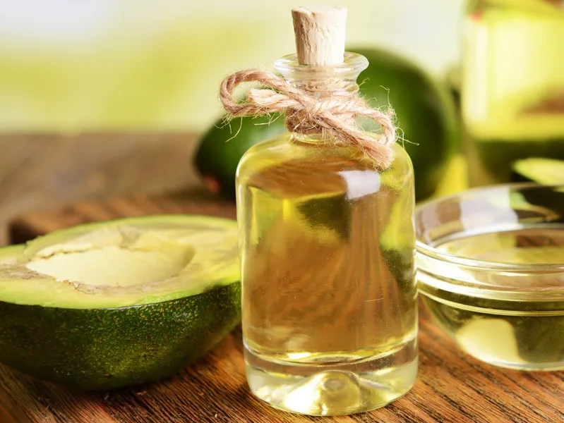 Avocado tagliato a metà accanto a una bottiglia di olio extravergine di oliva, ingredienti per una maschera capelli fai da te