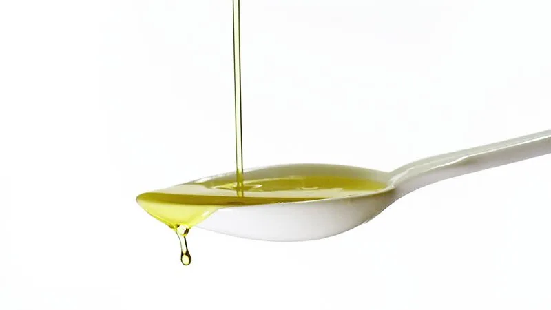 Cucchiaio con olio extravergine di oliva versato, simbolo della dose giornaliera consigliata