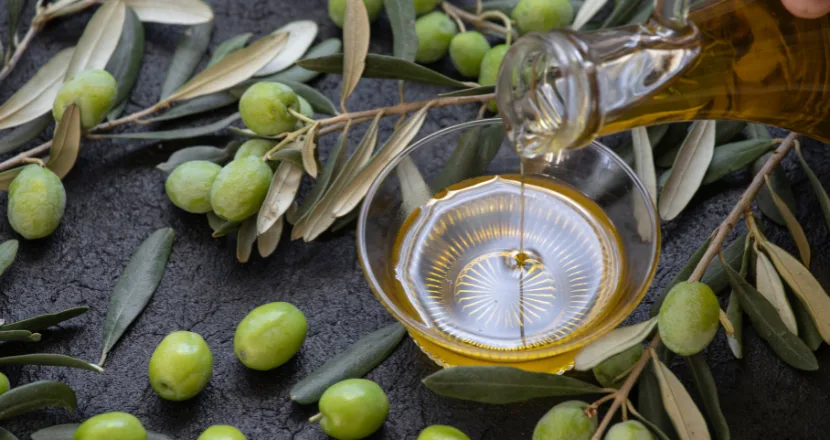 Bottiglia di olio extravergine di oliva versato accanto a olive fresche