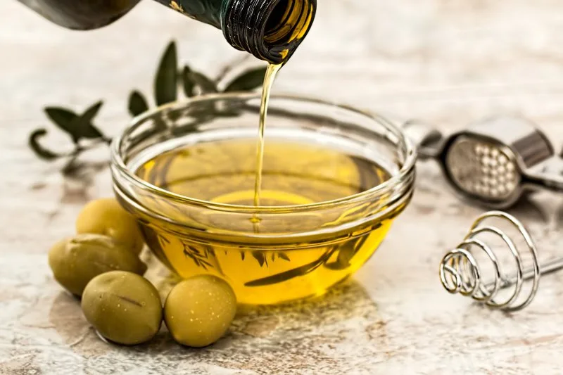 Bottiglia e ciotola di olive con olio extravergine, simbolo dell'equilibrio dei grassi nell'olio di oliva