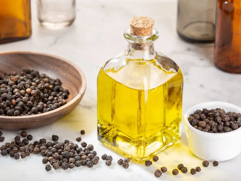 Bottiglia di olio extravergine di oliva e grani di pepe nero, ingredienti dell'olio da massaggio